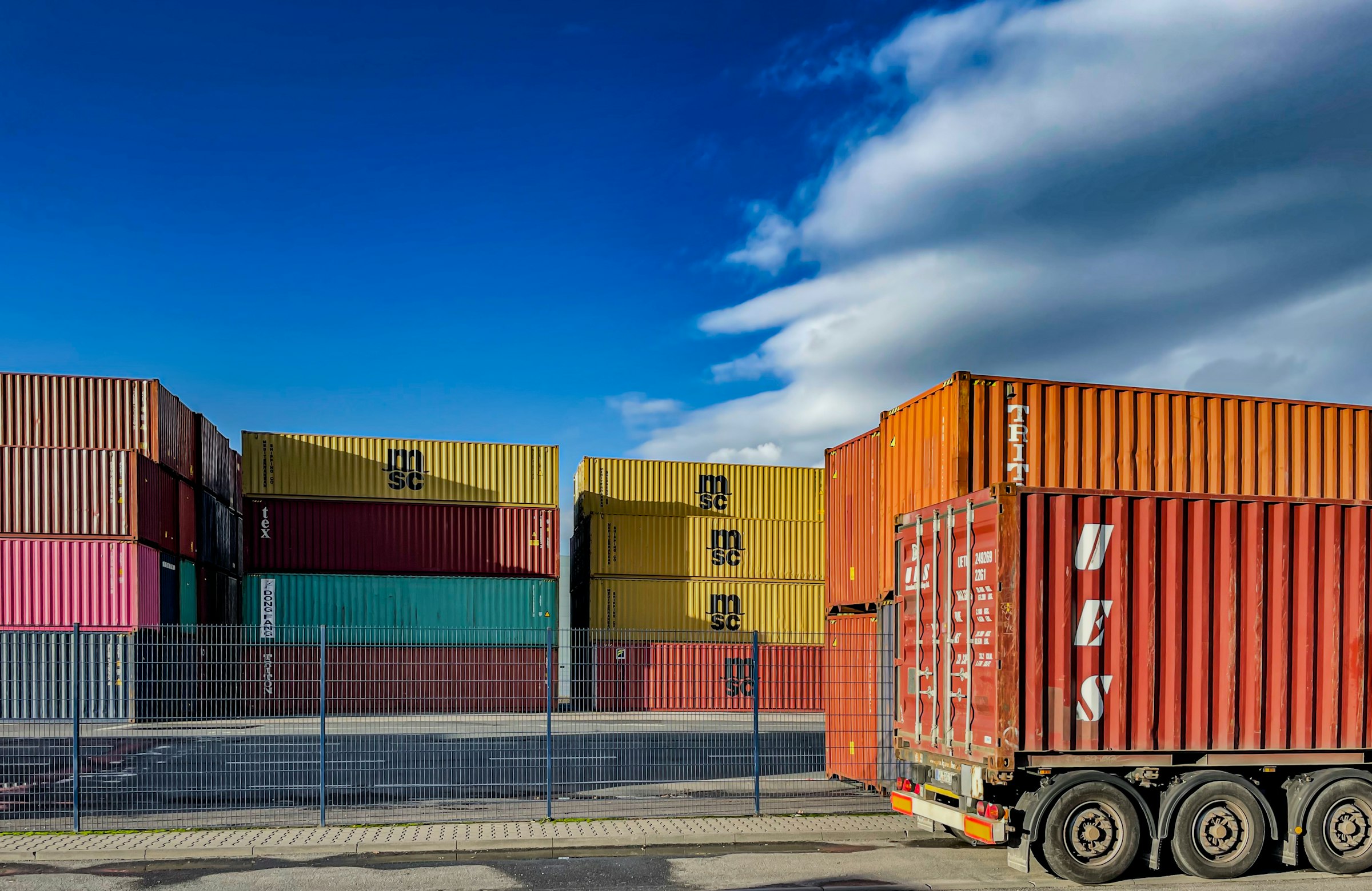 Shipping containers stacked at a container depot, with one loaded on a road chassis